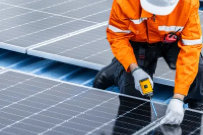 Technician in orange safety gear installing solar panels on rooftop.