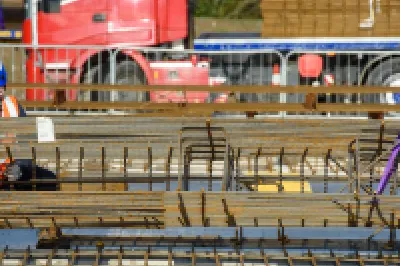 Construction workers on a bridge project with red truck visible in the background.