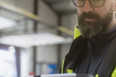 Construction worker in yellow hardhat and safety vest reviewing information on a tablet.