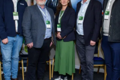 Group of people standing in a sports equipment room with jackets and athletic gear visible.