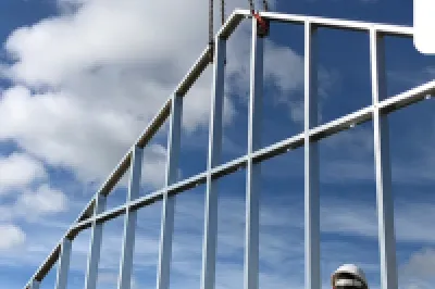 Construction worker in safety gear inspecting steel frame building structure against blue sky