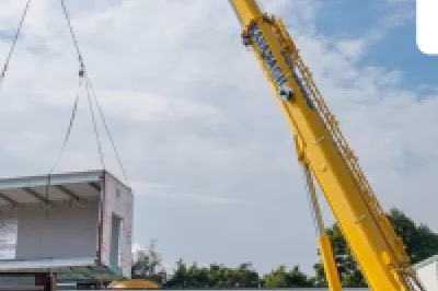 Yellow crane lifting a large modular structure at a construction site under blue sky.