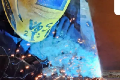 Welder in protective helmet working with bright blue sparks in industrial setting.