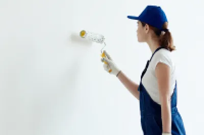 Person in blue cap and tank top painting a wall with a roller