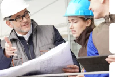 Construction professionals in blue hard hats examining building plans at a work site.