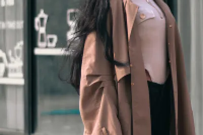 Stylish person in beige coat and sunglasses walking on street with shopping bag