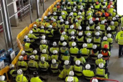 Workers in yellow safety vests in a large warehouse or retail facility with refrigeration units.