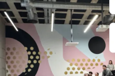 Audience seated in a modern lecture hall with geometric wall designs and digital screens.