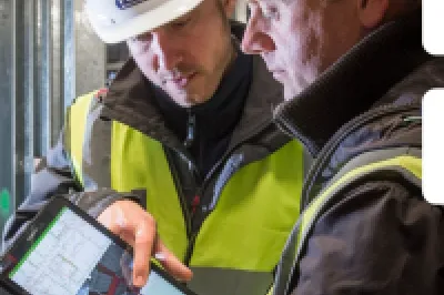 Construction worker in safety vest and hard hat reviewing information with supervisor at a construction site.