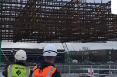 Construction workers in bright safety vests watching a large steel structure being lifted by a crane.