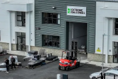 Aerial view of an industrial warehouse complex with solar panels, vehicles, and stacked materials outside.