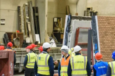 Group of workers in yellow safety vests observing construction work inside a large industrial building.