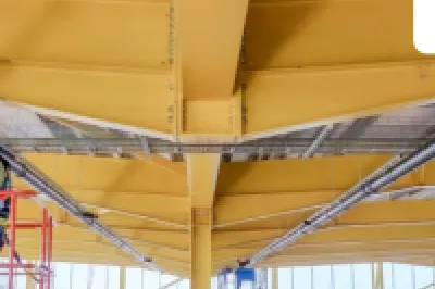 Worker on a yellow aerial lift platform inspecting a industrial building's ceiling structure.