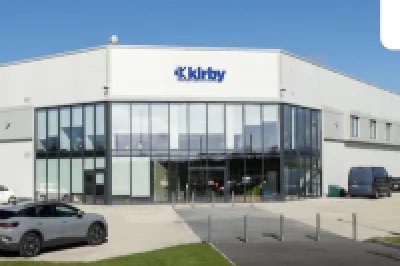 Large modern Kirby industrial building with parked cars outside under a partly cloudy sky.