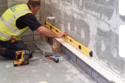 Worker in yellow vest using a level tool on a floor in a construction site, with two logos overlaid.