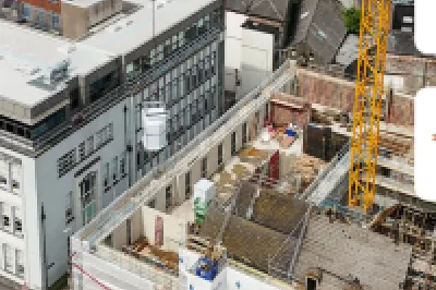 Aerial view of an active urban construction site with cranes, alongside a historic building.