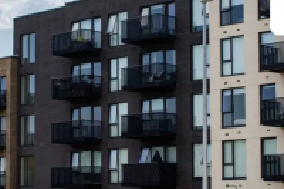 Modern multi-story apartment building with dark balconies under a blue sky, Extreme Balconies logo.