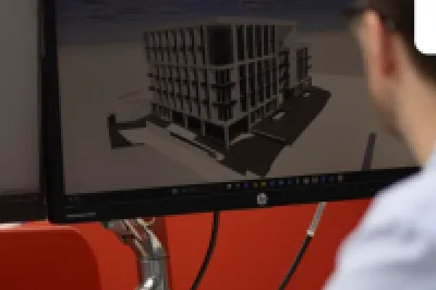 Man working at a computer displaying a 3D architectural building model in CAD software.