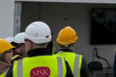 Group of construction workers in hi-vis vests and hard hats inspecting an outdoor facility.