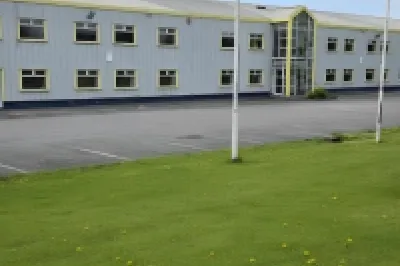 Two-story yellow office building with a green lawn and a red company sign in front.