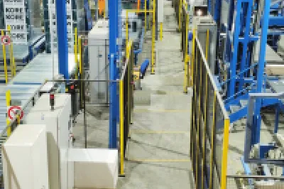 Industrial manufacturing facility with blue metal frames, conveyor systems, and white panels on the floor.