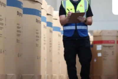 Worker in safety vest and helmet inspecting warehouse inventory with a tablet.