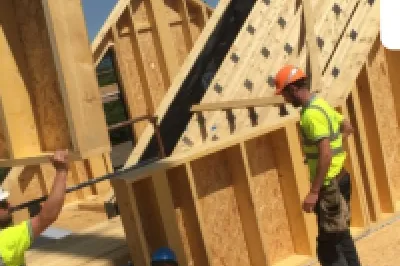 Construction workers in high-visibility vests assembling wooden wall frames for a new building.
