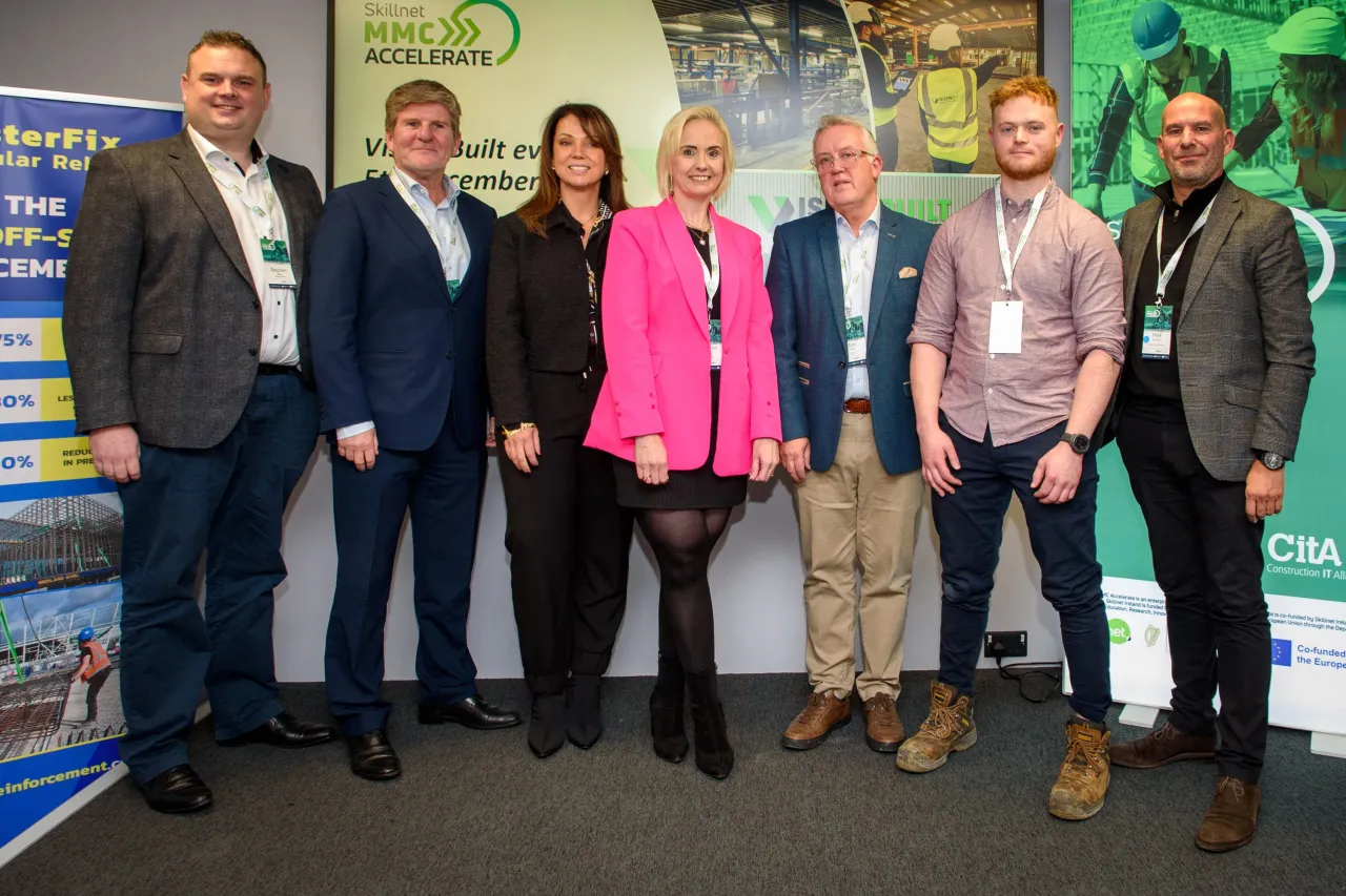 A group of business professionals posing together at a professional event with display banners in the background.