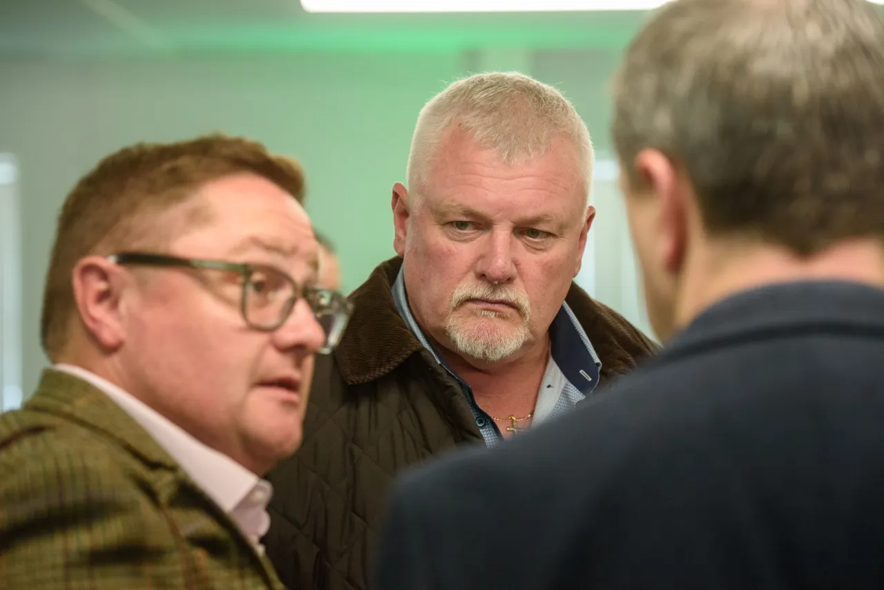 Three men in conversation, one wearing glasses and another with a gray beard.