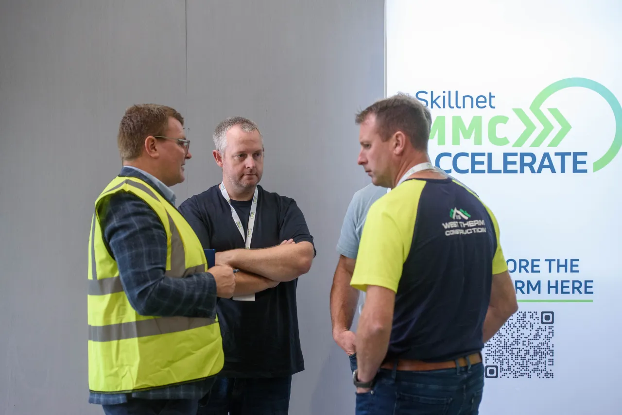 Three people in safety vests having a conversation in front of an "Accelerate" event sign.