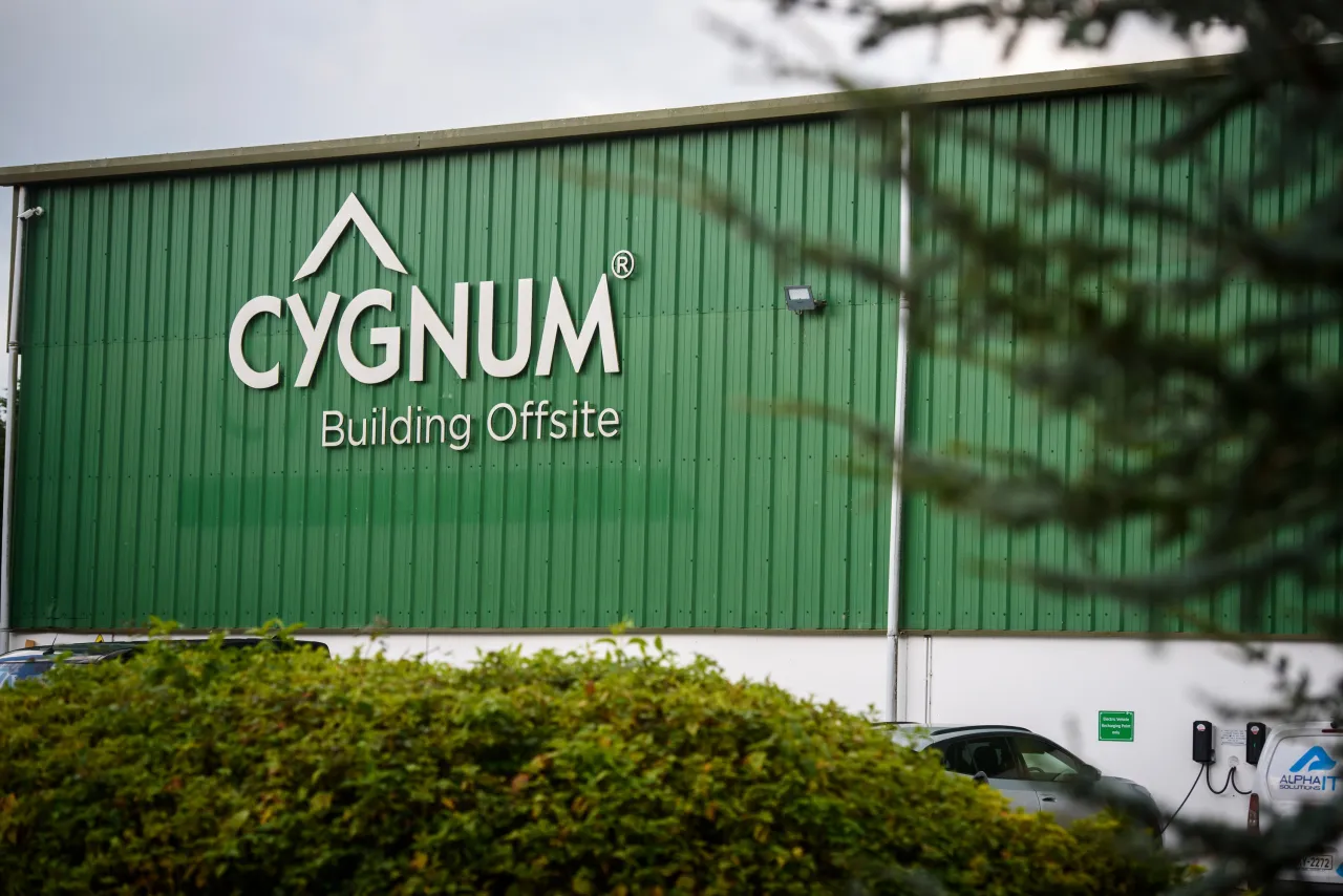 A green building with Cygnum logo, partially visible behind trees and bushes.