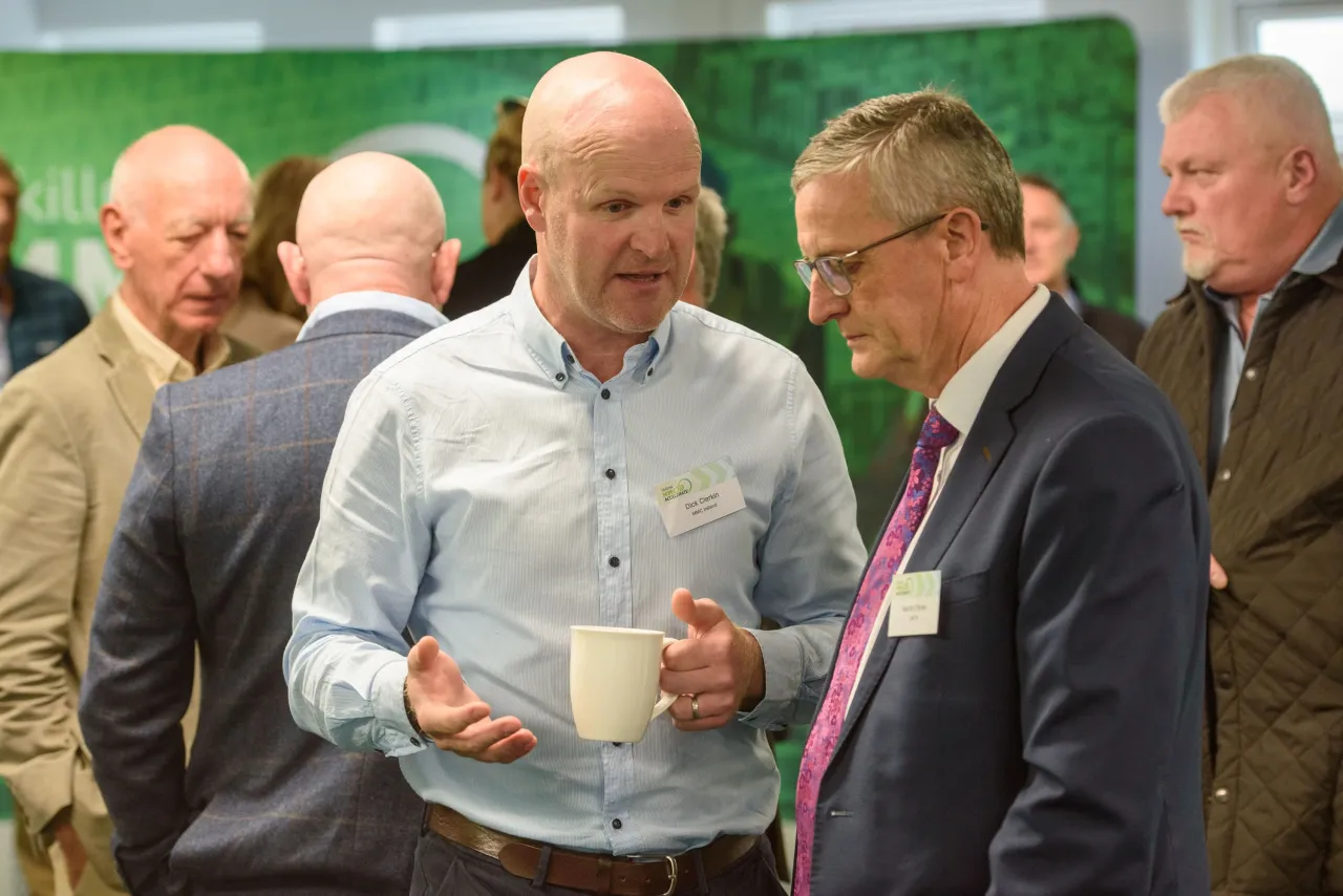 Two men in business attire examining documents at an indoor event or conference.