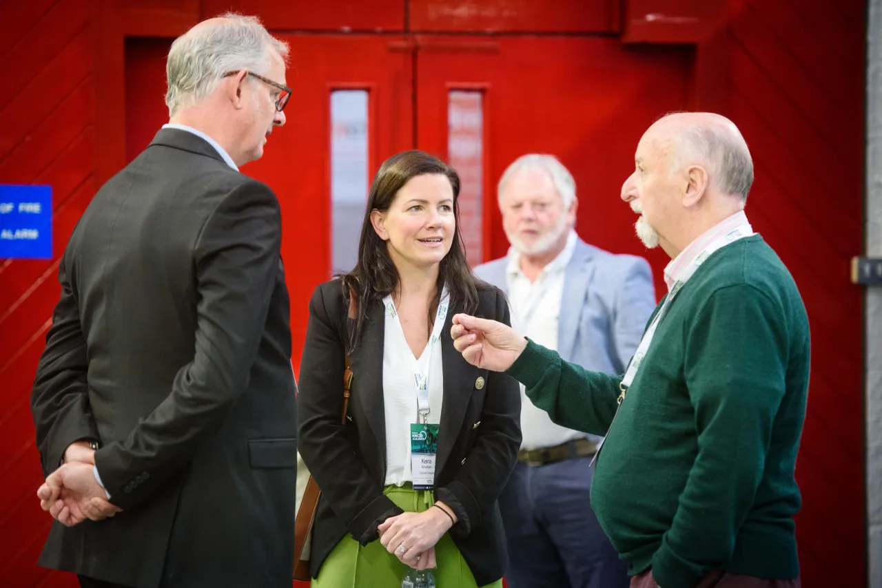 Group of people engaged in conversation against a bright red background.