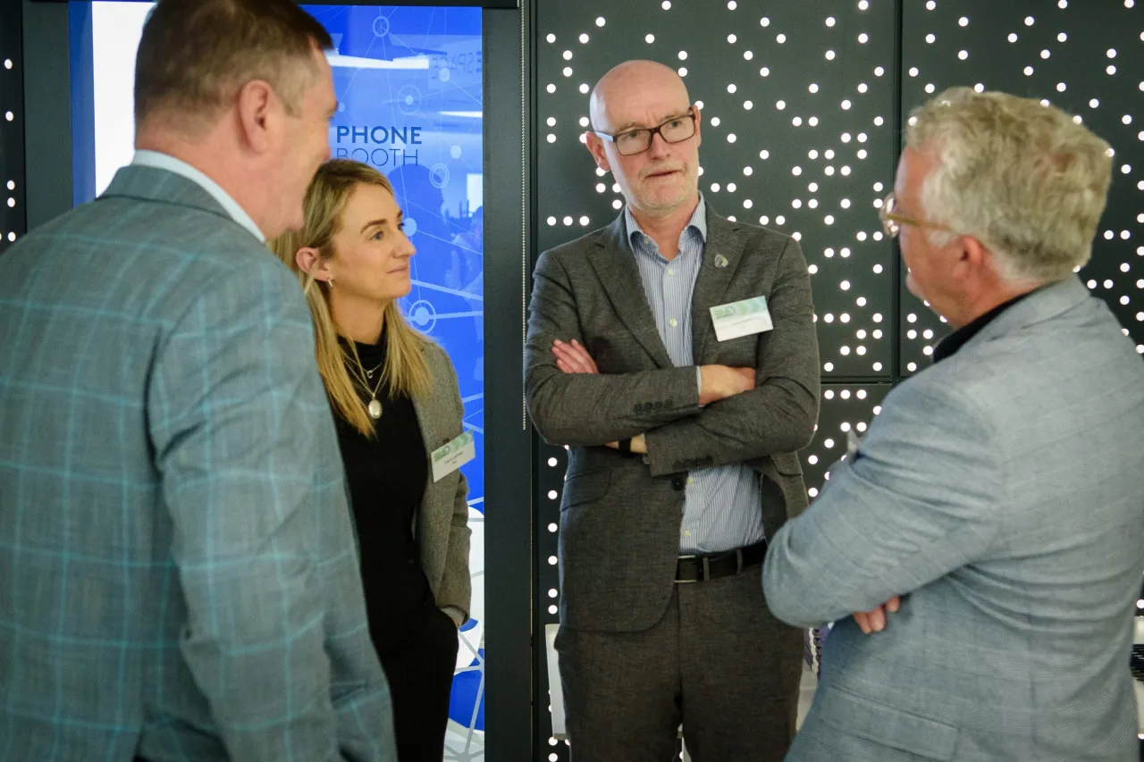 Professional conversation among four people in business attire against a patterned backdrop.
