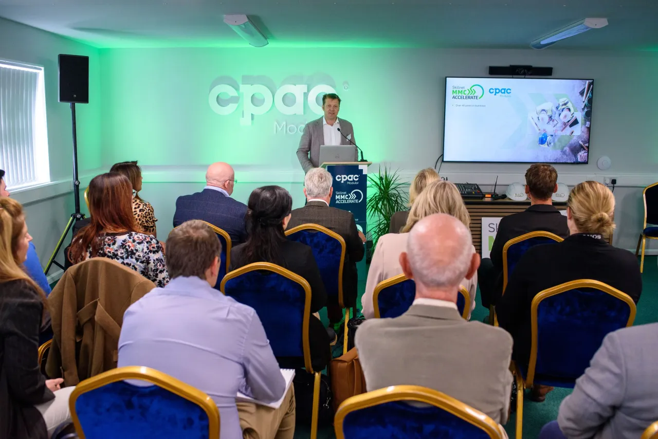 Speaker presenting at a business conference with green "cpre" logo projected on screen behind them.