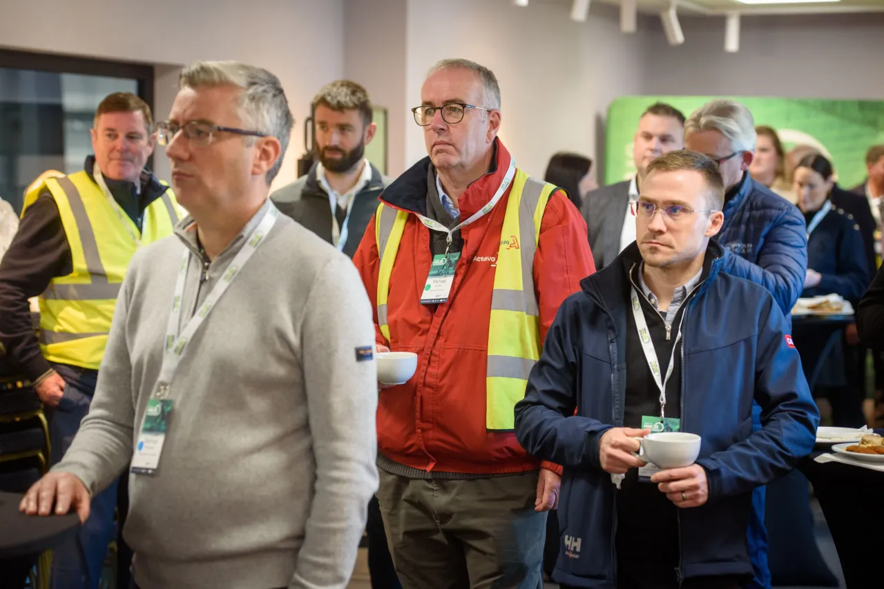 A group of workers in safety vests and casual clothing gathered in an indoor meeting or training area.