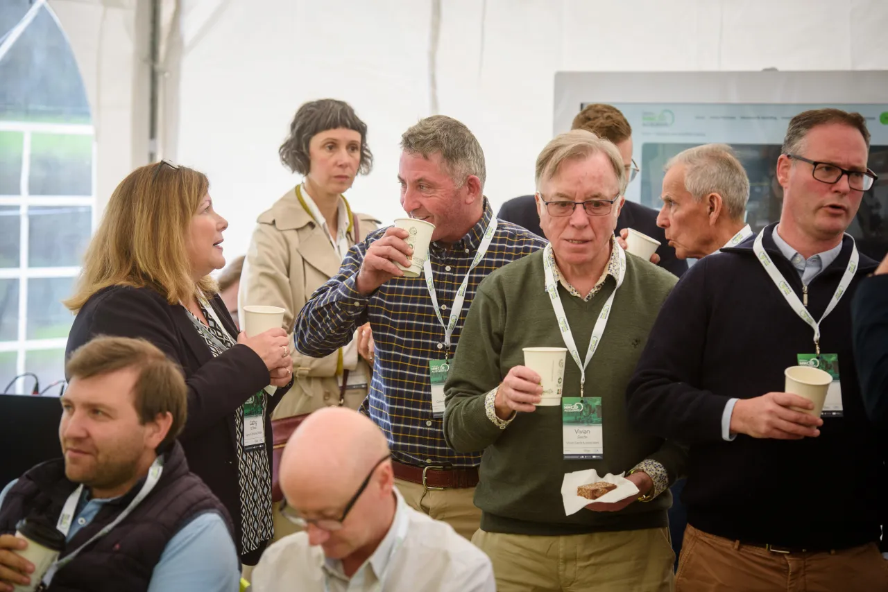 A group of people gathered at an event, holding drinks and socializing in a bright indoor space.