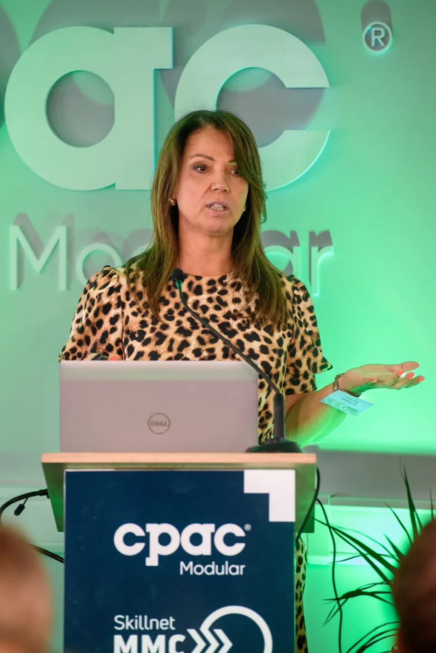 Woman in leopard print blouse presenting at a podium with CPAC logo, green backdrop.