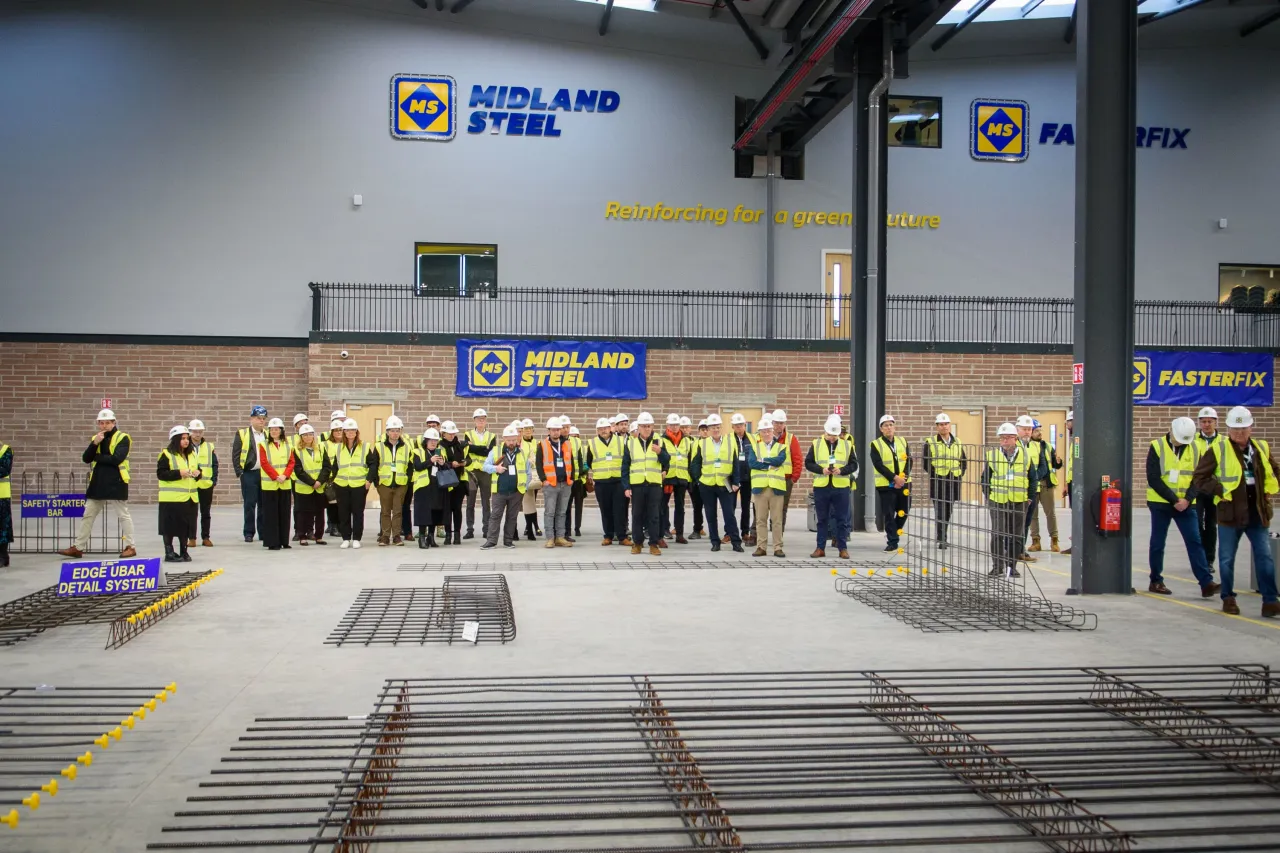 A line of construction workers in high-visibility vests standing inside an industrial facility with concrete floors.