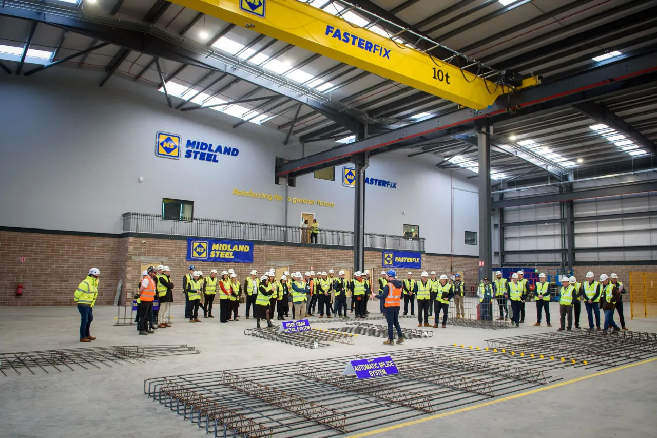 Workers in safety vests gathered in an industrial facility with a yellow overhead crane.