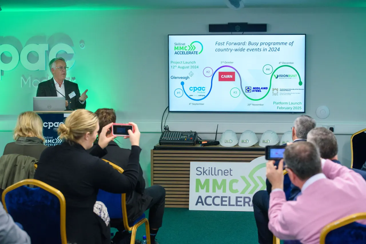 Presenter giving a talk with a PowerPoint slide showing a process flow diagram with green lighting.