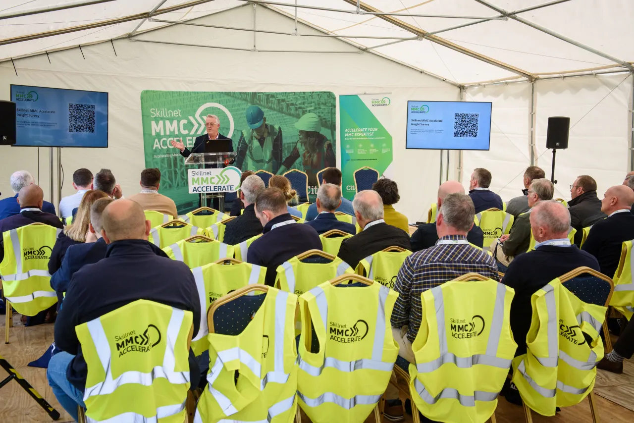 Group of workers in high-visibility vests attending a presentation in a white tent structure.