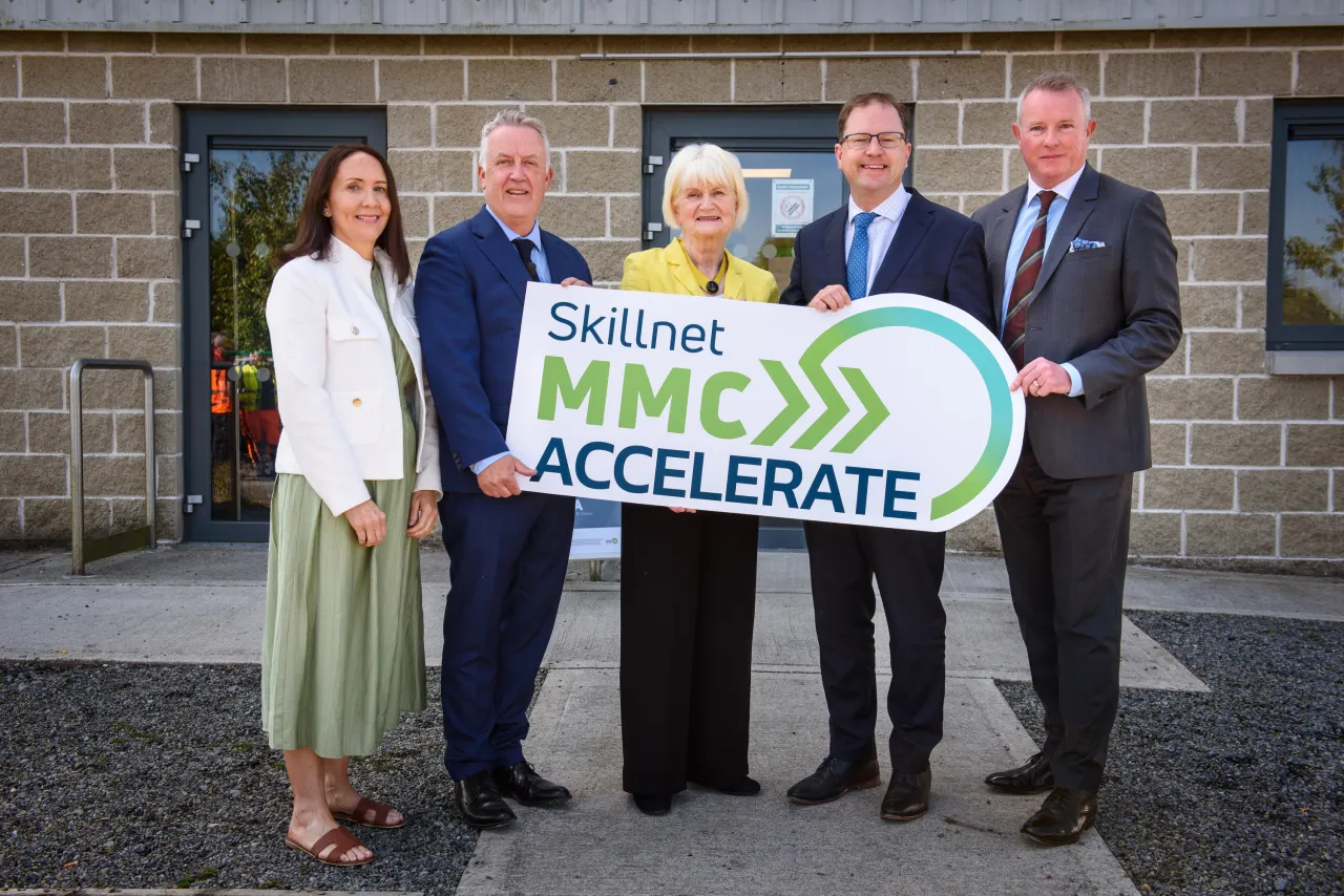 Five people standing outdoors holding a large APEX Accelerate banner in front of a building.