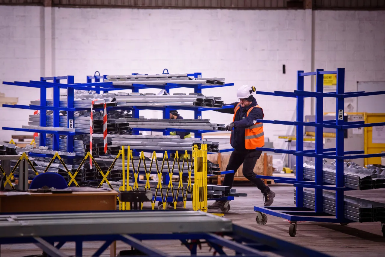 Worker in orange safety vest walking through industrial warehouse with blue storage racks