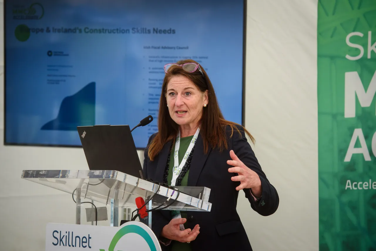 A woman in business attire presenting with a laptop at a conference or event.