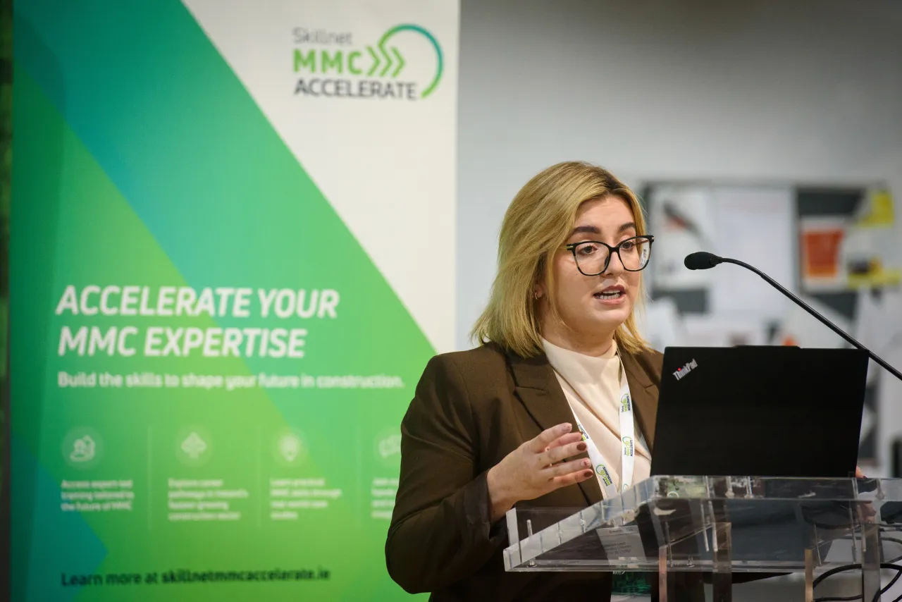 A woman in glasses speaking at a podium with a green APAC Metrology event banner behind her.