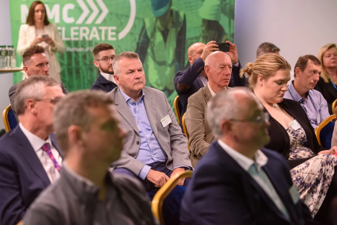 Attentive audience members listening at a conference with green backdrop lighting.
