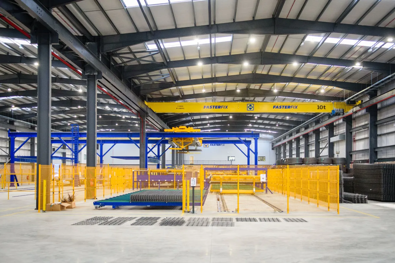 Industrial warehouse interior with overhead crane, steel beams, and yellow machinery on concrete floor.