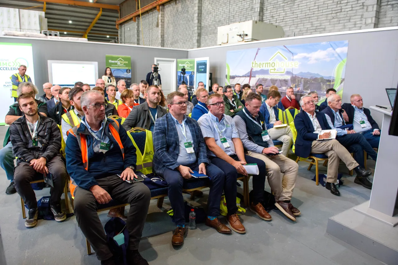 Group of attendees seated at an industrial conference or presentation event with colorful backdrop displays.