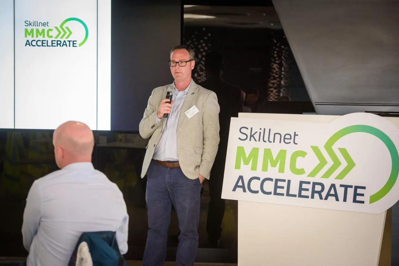 A speaker presenting at a business event with "Solimar MPOWER ACCELERATE" sign visible.